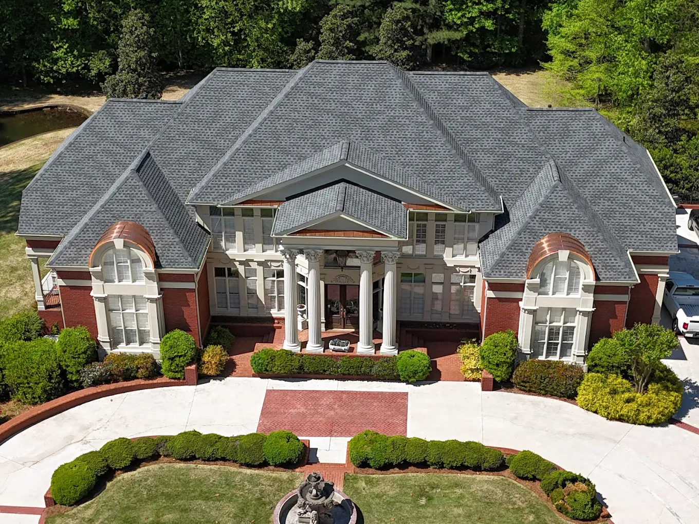 Aerial view of a completed brand-new architectural shingle roof on a large columned brick estate with a circular drive